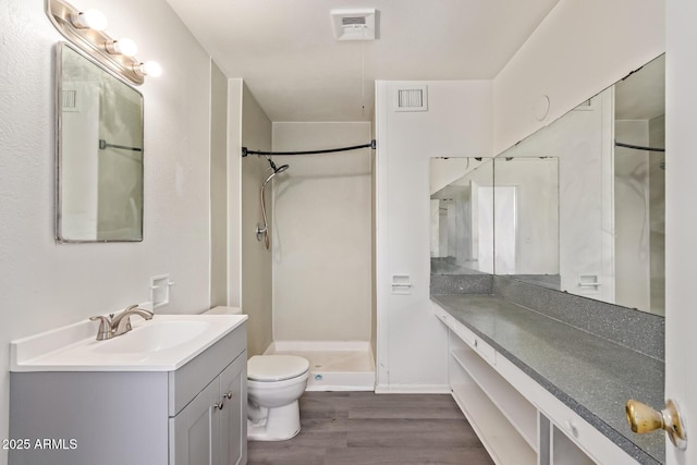 bathroom with toilet, vanity, wood finished floors, walk in shower, and visible vents