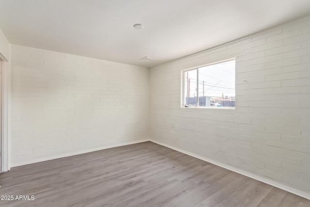 spare room featuring wood finished floors and brick wall
