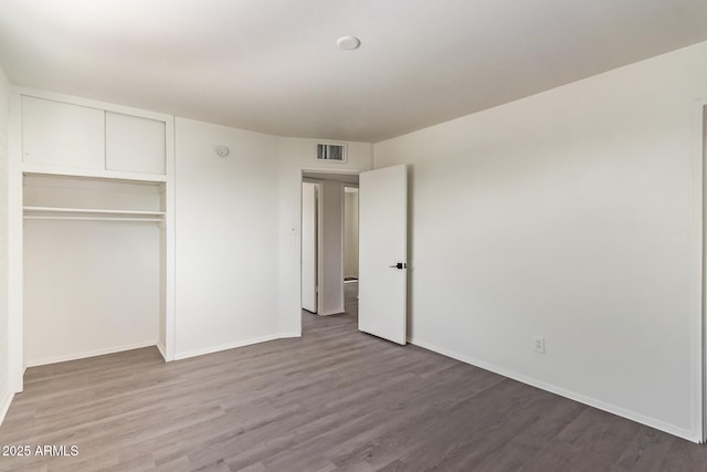unfurnished bedroom featuring wood finished floors, baseboards, a closet, and visible vents