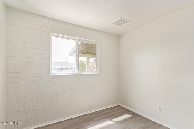 unfurnished room with baseboards, visible vents, brick wall, and wood finished floors