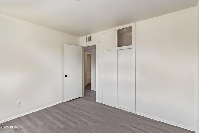 unfurnished bedroom with a closet, baseboards, visible vents, and wood finished floors