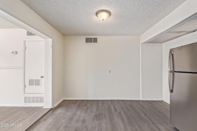 spare room featuring wood finished floors, a textured ceiling, and visible vents