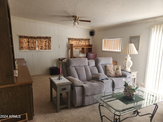 carpeted living room with a textured ceiling, wooden walls, ceiling fan, and crown molding