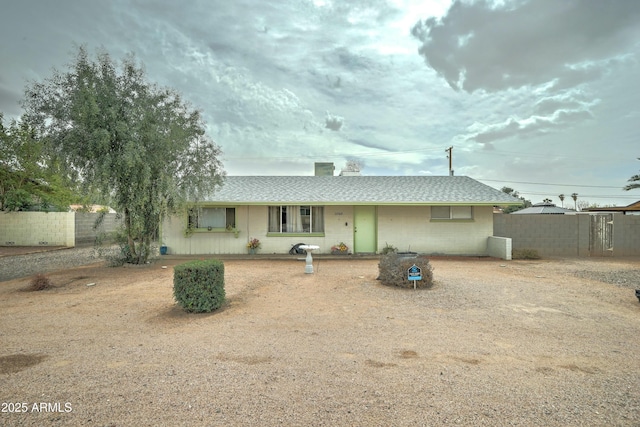 view of front of property with a chimney, a shingled roof, concrete block siding, and fence