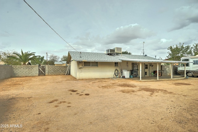 back of property with a gate, fence, concrete block siding, a shingled roof, and central AC unit