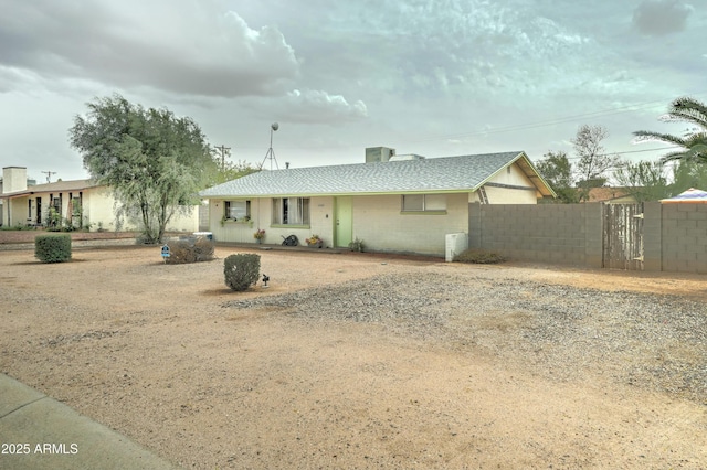 view of front facade featuring gravel driveway, concrete block siding, fence, and a shingled roof