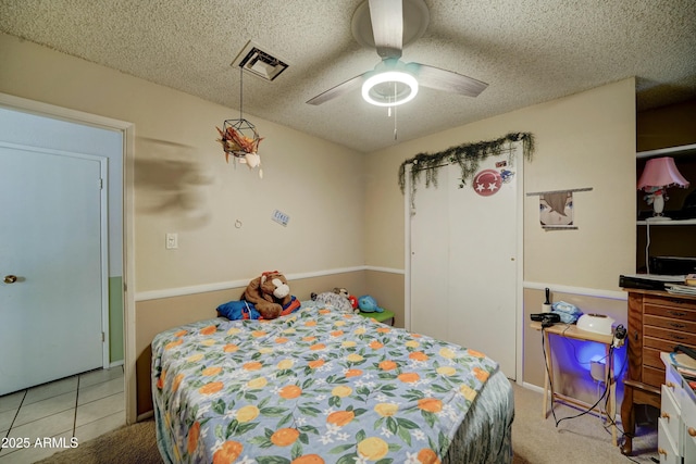 bedroom with carpet, a ceiling fan, visible vents, tile patterned flooring, and a textured ceiling