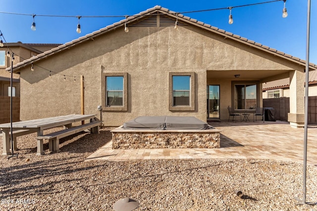 rear view of property featuring a covered hot tub and a patio