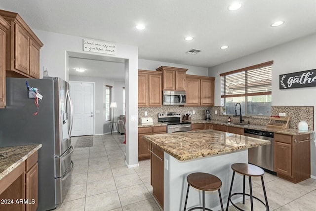 kitchen with a center island, sink, stainless steel appliances, light stone counters, and a breakfast bar area