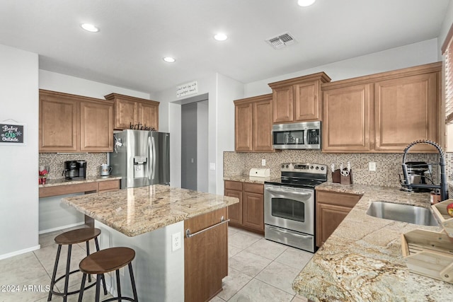 kitchen with light stone counters, a kitchen bar, decorative backsplash, a kitchen island, and appliances with stainless steel finishes