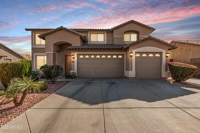 mediterranean / spanish-style home with a tile roof, stucco siding, concrete driveway, and a garage