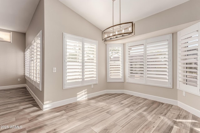 unfurnished dining area with baseboards, light wood finished floors, a chandelier, and vaulted ceiling