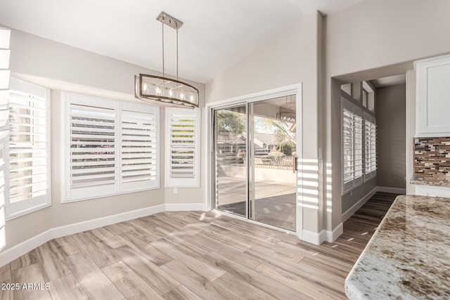 unfurnished dining area featuring light wood-type flooring, baseboards, lofted ceiling, and a chandelier