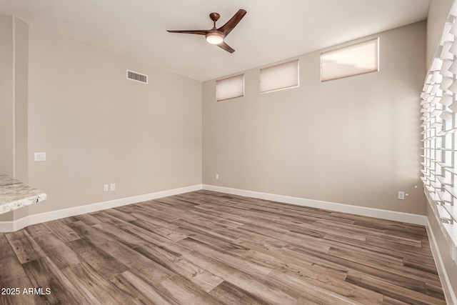 empty room with baseboards, a ceiling fan, wood finished floors, and visible vents