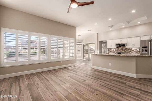unfurnished living room with a healthy amount of sunlight, baseboards, a ceiling fan, and wood finished floors