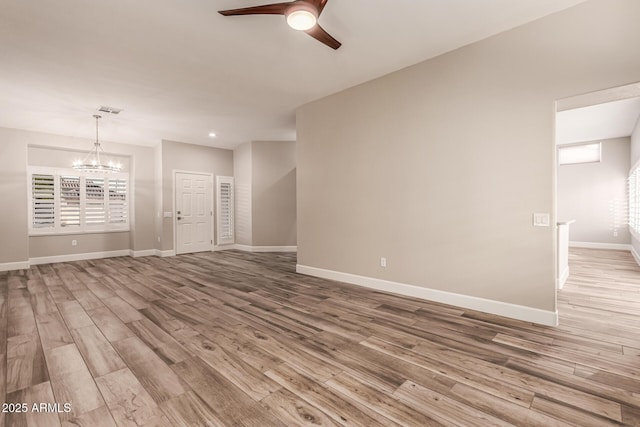 unfurnished living room with baseboards, ceiling fan with notable chandelier, wood finished floors, and visible vents
