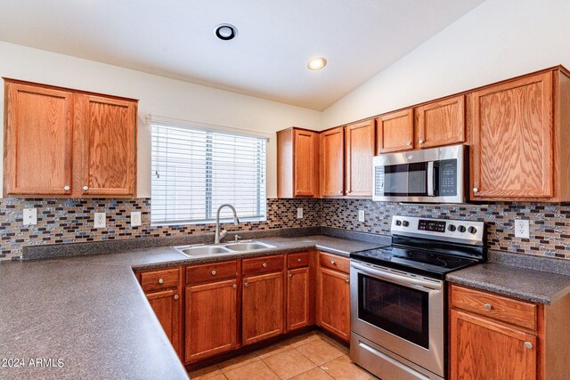 kitchen with appliances with stainless steel finishes, sink, vaulted ceiling, decorative backsplash, and light tile patterned floors