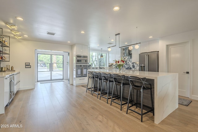 kitchen featuring visible vents, modern cabinets, a kitchen breakfast bar, light wood-style floors, and stainless steel fridge with ice dispenser