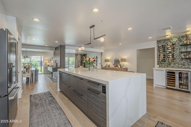 kitchen featuring light wood-type flooring, modern cabinets, beverage cooler, stainless steel fridge, and hanging light fixtures