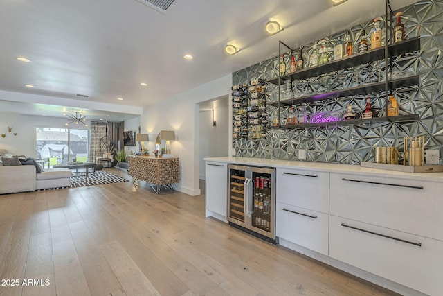 bar featuring wine cooler, recessed lighting, a bar, and light wood-style floors