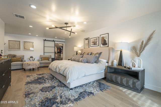 bedroom with wood finished floors, visible vents, recessed lighting, a walk in closet, and a barn door