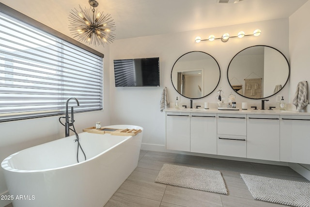 full bath featuring a sink, a freestanding tub, an inviting chandelier, and double vanity