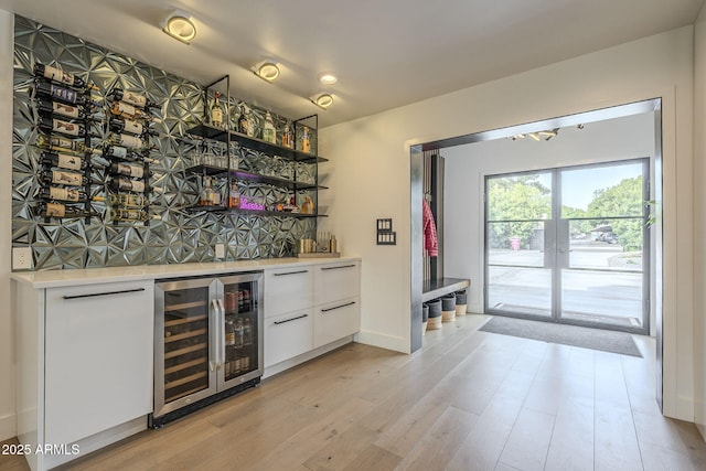bar with wine cooler, light wood-type flooring, decorative backsplash, french doors, and a bar
