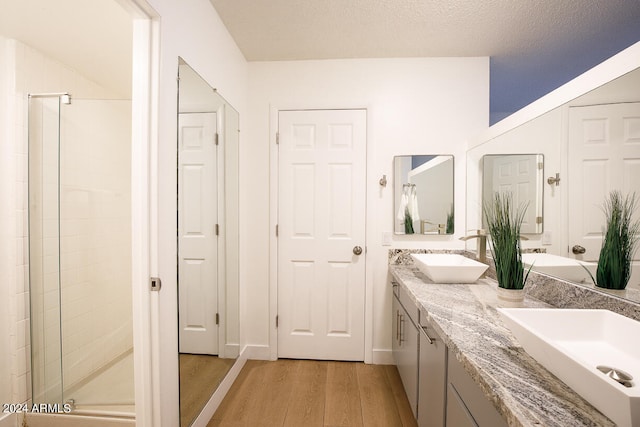 bathroom with a textured ceiling, wood-type flooring, a shower with door, and vanity