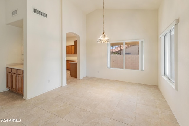 unfurnished dining area with a healthy amount of sunlight, light tile patterned floors, high vaulted ceiling, and a chandelier