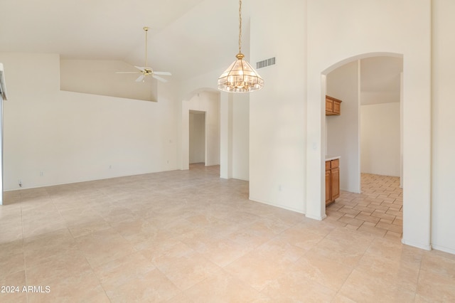 empty room featuring ceiling fan with notable chandelier and high vaulted ceiling