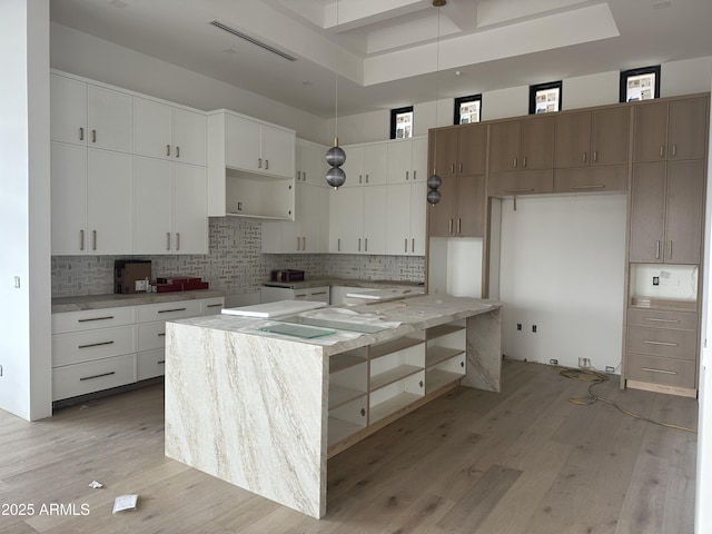 kitchen featuring visible vents, backsplash, a kitchen island, light wood-style floors, and white cabinets