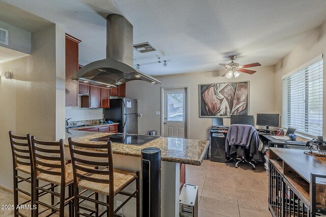 kitchen featuring a healthy amount of sunlight, black electric cooktop, freestanding refrigerator, and island range hood