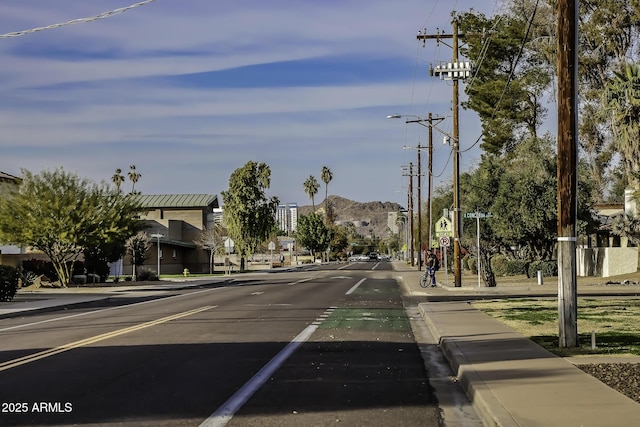 view of road featuring sidewalks, street lights, a mountain view, and curbs