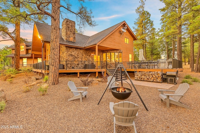 7500 E Old Walnut Canyon Rd, Flagstaff, AZ 86004 - back of house at dusk featuring stone siding, a chimney, an outdoor fire pit, a deck, and a patio area