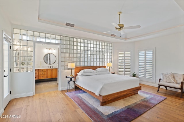 bedroom featuring a tray ceiling, ensuite bath, ceiling fan, and light hardwood / wood-style flooring