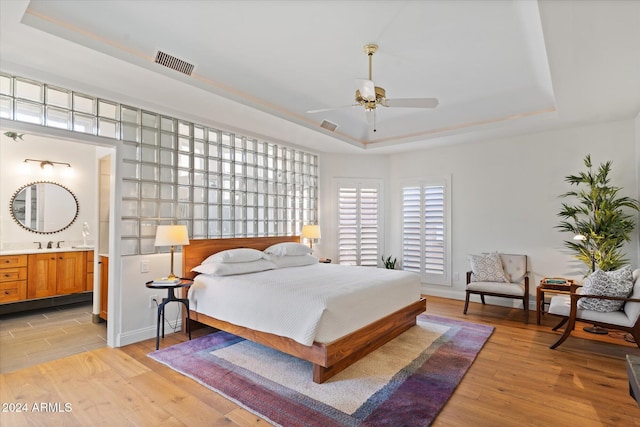 bedroom with a tray ceiling, ensuite bath, ceiling fan, and light hardwood / wood-style floors