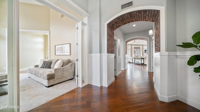 hall featuring visible vents, a wainscoted wall, dark wood-type flooring, arched walkways, and a decorative wall