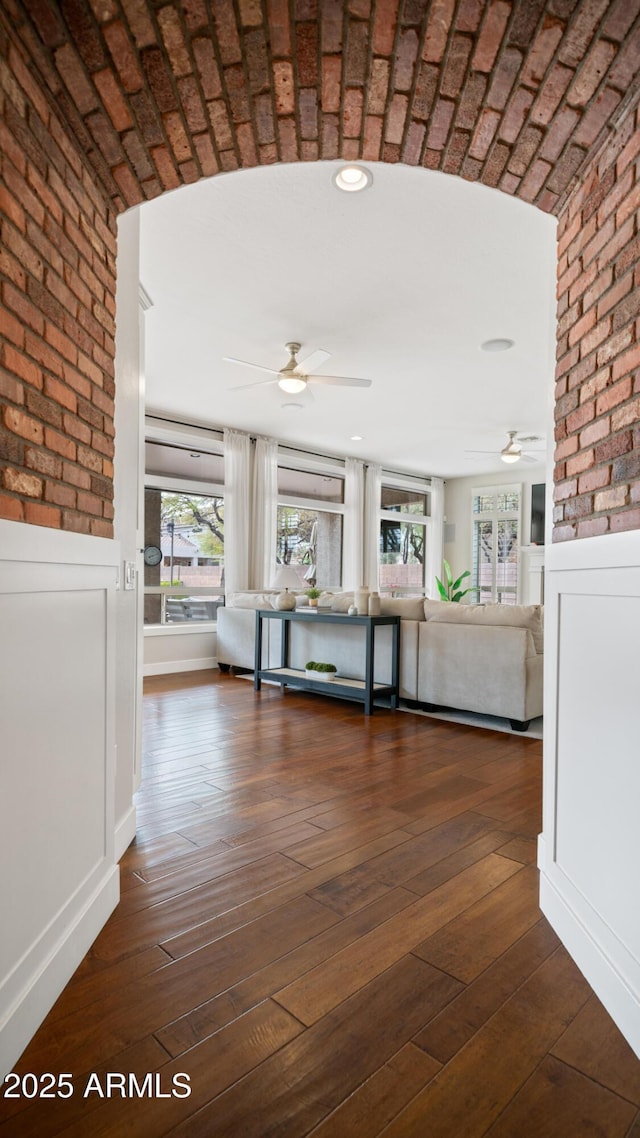 corridor with dark wood-type flooring, a wainscoted wall, and brick wall