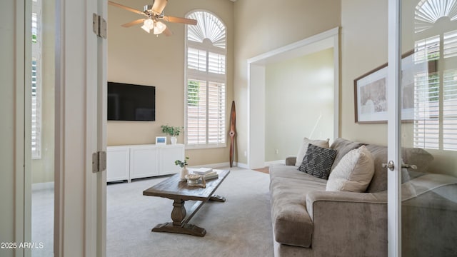 carpeted living area with a high ceiling, baseboards, and ceiling fan