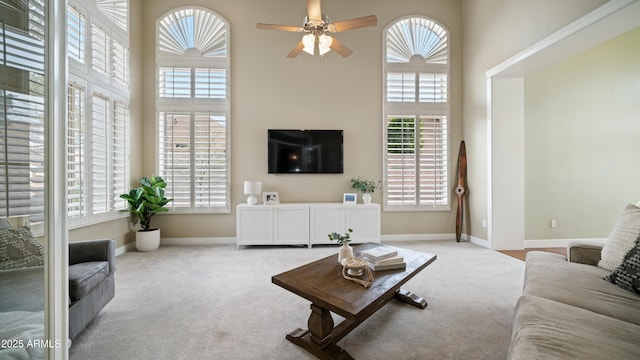 living room with baseboards, carpet floors, a towering ceiling, and a ceiling fan