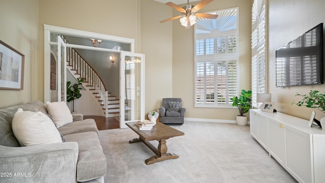 living area with a ceiling fan, baseboards, a high ceiling, stairs, and light carpet