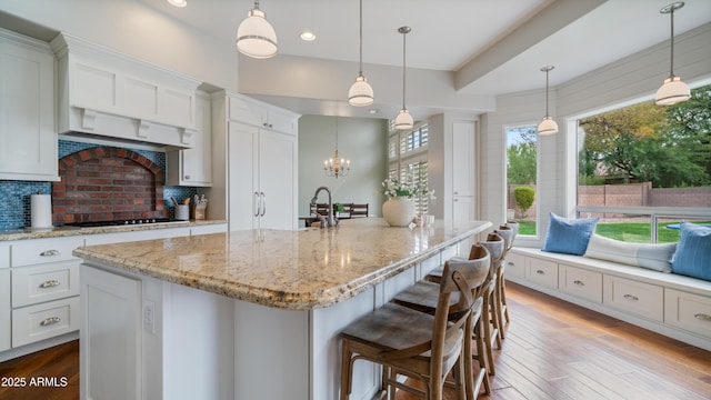 kitchen with light stone counters, wood finished floors, gas stovetop, decorative backsplash, and white cabinetry