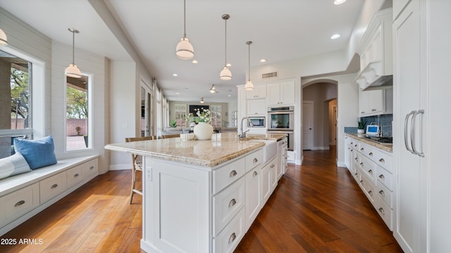 kitchen with tasteful backsplash, visible vents, arched walkways, white cabinetry, and a sink