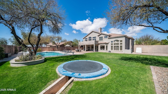 rear view of house with a fenced in pool, a trampoline, a chimney, a fenced backyard, and a patio area