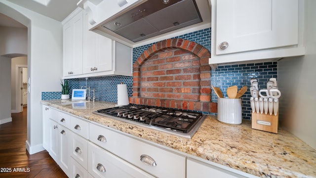 kitchen featuring decorative backsplash, stainless steel gas stovetop, exhaust hood, and arched walkways