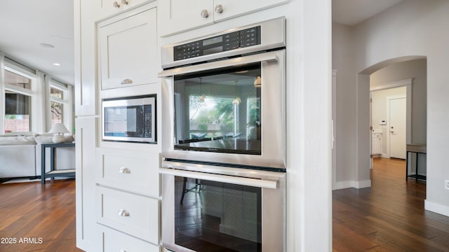 kitchen featuring dark wood-style floors, baseboards, arched walkways, stainless steel appliances, and white cabinets