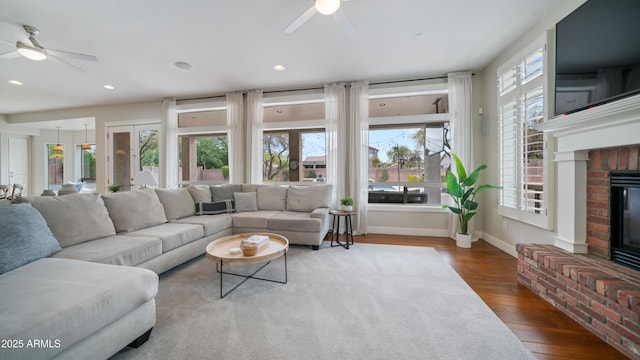 living room with a brick fireplace, wood finished floors, baseboards, and ceiling fan