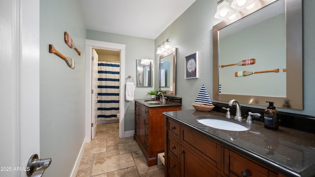 bathroom featuring stone tile flooring, two vanities, baseboards, and a sink