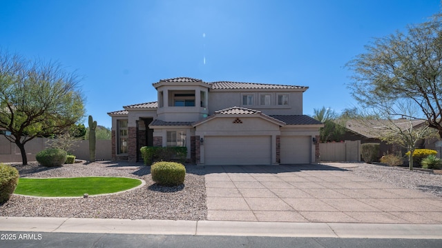 mediterranean / spanish house with fence, concrete driveway, a tile roof, stucco siding, and stone siding