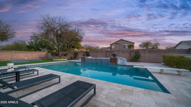 pool at dusk featuring a pool with connected hot tub, a patio area, and a fenced backyard